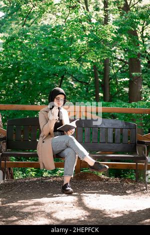 Muslimische Frau beim Lesen auf einer Bank während des schönen Frühlingstages Stockfoto