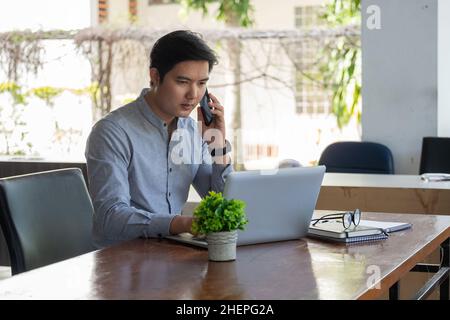 Porträt des jungen asiatischen Mann freiberuflich online arbeiten von zu Hause aus mit Laptop-Computer während Anruf Telefon. Quaratine Coronavirus, Technologie-Startup Stockfoto