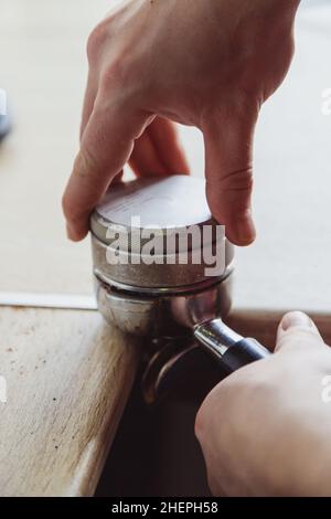 Nahaufnahme des Mannes mit einem Sabotagekontakt, um gemahlenen Kaffee in einen Portafilter zu pressen Stockfoto