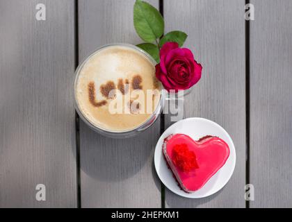 Red Heart Kuchen zum Valentinstag mit einer Tasse Kaffee mit dem Wort Liebe auf dem Milchschaum geschrieben. Blick von oben. Positives Denken, Guten Morgen, Stockfoto