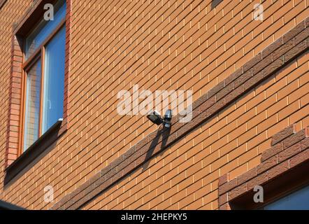 Motion Flood LED-Licht auf Haus Ziegelwand im Freien. Auswählen und Installieren der Bewegungsmelderbeleuchtung. Bewegungssensor. Stockfoto