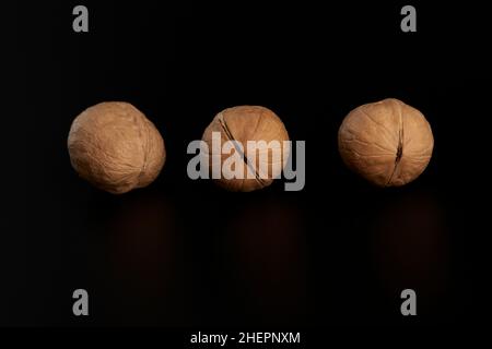 Drei Schalenwalnüsse liegen in einer Reihe auf schwarzem Hintergrund. Stockfoto