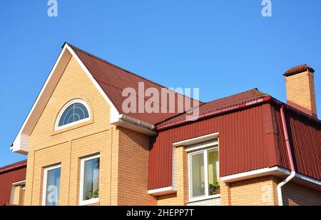 Dachboden außen mit Asphaltschindeln und Kunststoff-Regenrinnen-System. Nahaufnahme der Dachart des Mansard-Hauses. Stockfoto