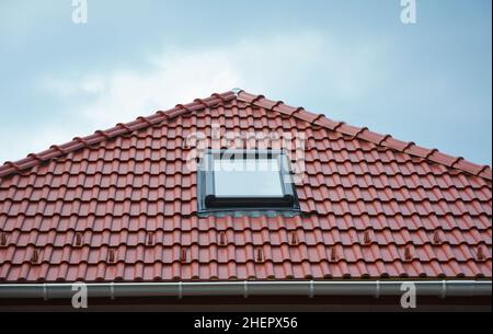 Nahaufnahme des Dachfensters des Hauses, der Oberlichter des Sonnentunnels oder des Oberlichts nach Regen auf dem Dach aus roten Keramikfliesen. Dachgeschoss Dachfenster Lösung im Freien. Stockfoto