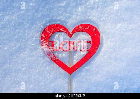 Eine herzförmige Figur mit dem Wort Liebe liegt auf dem Schnee. Liebesbotschaft in romantischer Form Stockfoto