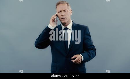 Gestresster Geschäftsmann im Gespräch auf Handy isoliert auf grau Stockfoto