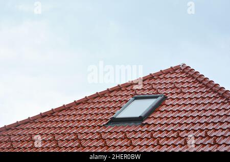 Wunderschönes Hausdachfenster, Sonnentunnel-Oberlichter oder Dachfenster nach Regen auf rotem Keramikfliesen-Dach. Dachgeschoss Dachfenster Lösung im Freien. Stockfoto