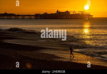 Brighton, West Sussex, 12/01/2022, Einheimischer Schwimmer, der von einem frühen Morgenschwimmen am Brighton Beach mit dem Palace Pier im Hintergrund während des Sonnenaufgangs in Brighton, West Sussex, zurückkehrt Stockfoto