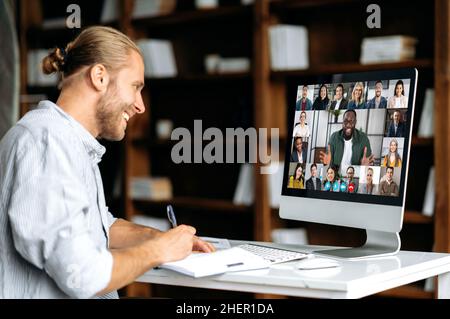 Intelligenter moderner Kaukasier, Student oder Freiberufler, hört sich ein Online-Webinar an, hält Vorträge, notiert Informationen und studiert per Videokonferenz aus der Ferne. E-Learning-Konzept Stockfoto