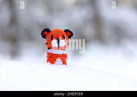 Gestrickter Spielzeug-Tiger auf Schnee in einem Wald. Hintergrund für Grußkarte zur Feier des neuen Jahres 2022 des Tigers nach dem chinesischen Kalender Stockfoto