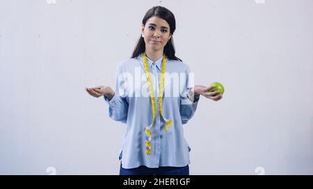 Verwirrt Frau Vergleich von Vitaminen und Apfel isoliert auf grau, Stock Bild Stockfoto