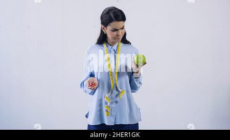 Brunette Frau Vergleich von Vitaminen und frischem Apfel isoliert auf grau, Stock Bild Stockfoto