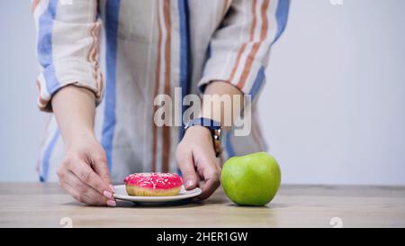 Beschnittene Ansicht der Frau, die Platte mit Donut in der Nähe von Apfel hält, isoliert auf grauem, stockem Bild Stockfoto