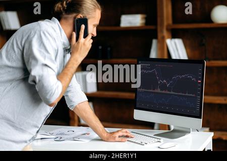 Investitionen, Handel an der Börse. Kaukasischer Mann Händler Investor, spricht auf dem Handy, Analyse Kryptowährung Finanzmarkt, schaut auf Computer, Trading-Daten Index Chart Graph auf pc-Bildschirm Stockfoto
