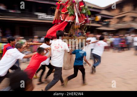 Jugendliche, die während der nepalesischen Neujahrsfeierlichkeiten (Bisket Jatra) im UNESCO-Weltkulturerbe Bhaktapur einen Khat (Palanquin) durch die Straße tragen. Stockfoto