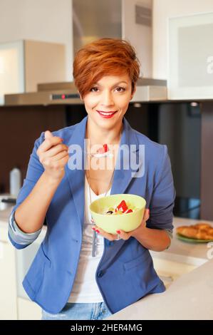 Lächelnde junge Frau, die in der modernen Küche frisches Obst isst Stockfoto