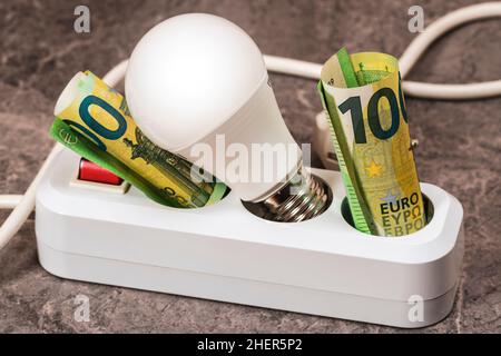 Euro Money und LED-Glühlampe in einer Verlängerungsbuchse eingesetzt. Steigende Stromkosten für Geschäfts- und Privatkunden. Steigen Sie ein Stockfoto