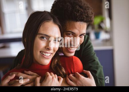 Porträt eines fröhlichen jungen Birazialmannes, der seine Freundin von hinten umarmt Stockfoto