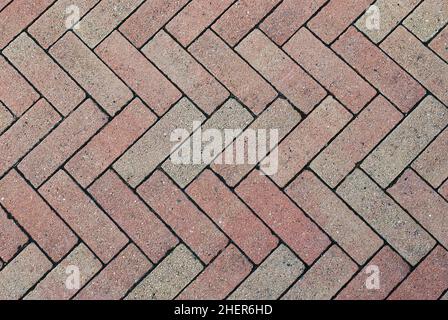 Nahaufnahme einiger verwitterter, roter Herringbone-Block-Pflastersteine, die ein symmetrisches Zick-Zack-Muster bilden Stockfoto