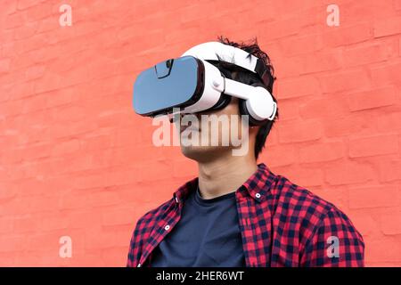 Porträt eines gelangweilten jungen asiatischen Mannes mit 3D Zuschauern mit Kopfhörern im Freien - Technologie und Videospiel süchtig oder futuristisches Konzept Stockfoto