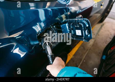 Hand hält einen Schlauch, der in ein Auto aus Flüssiggas (Flüssiggas) eingesteckt ist, an einer Tankstelle in einem metallisch-blauen Auto. Tanken, Tankstelle, Öko Stockfoto
