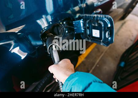 Hand hält einen Schlauch, der in ein Auto aus Flüssiggas (Flüssiggas) eingesteckt ist, an einer Tankstelle in einem metallisch-blauen Auto. Tanken, Tankstelle, Öko Stockfoto