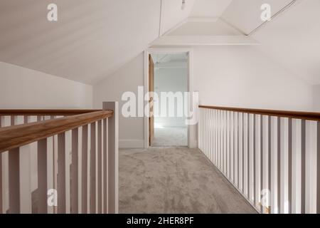 Cowlinge, Suffolk, England - 28. März 2019: Galleried Landung mit einfachen Spindeln, Eichenhandlauf, offene Tür zum Schlafzimmer und Teppich Stockfoto