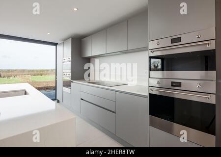 Cowlinge, Suffolk, England - 28. März 2019: Minimalistische, graue Küche mit weißen Granitoberflächen, Einbaugeräten und eingenem Waschbecken Stockfoto