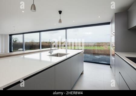 Cowlinge, Suffolk, England - 28. März 2019: Minimalistische, graue Küche mit weißen Granitoberflächen, Einbaugeräten und eingenem Waschbecken in op Stockfoto
