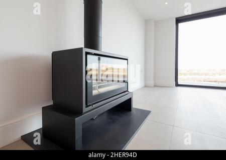 Cowlinge, Suffolk, England - 28. März 2019: Generischer Multi-Fuel-Kamin mit schwarzem Ofen auf Granitherd und passendem schwarzen Rohrkamin Stockfoto