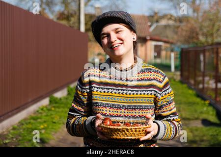 Glücklich lächelnde Frau hält Korb mit farbigen roten Eiern, Osterfeiertagskonzept. Hände mit modernen bemalten ostereiern. Junge Hipster Millennial wom Stockfoto