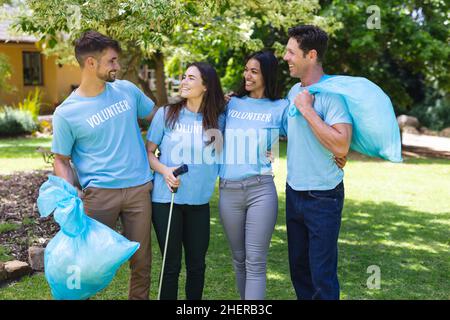 Glückliche multirassische Freiwillige sammeln Müll in Plastiktüten während der Reinigung im Park Stockfoto