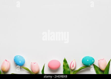 Osterkomposition auf grauem pastellfarbenem Hintergrund. Tulpen und bunte Eier. Rand flach Lay Draufsicht Kopieplatz Stockfoto