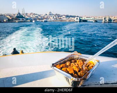 Fleischgericht mit Kunststoffgabel steht auf dem Stand im Fährschiff mit Touristen und istanbul Stadt im Hintergrund. Essen in der Türkei mitnehmen und verschwenden Stockfoto