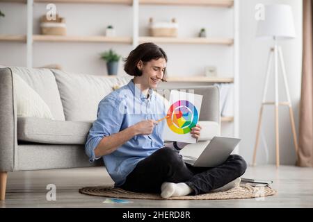 Aufgeregter männlicher Art-Manager, der von zu Hause aus eine Videokonferenz abhalten, Farbpalette halten und mit einer Laptop-Webcam sprechen kann Stockfoto