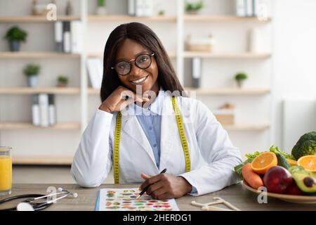 Porträt eines glücklichen afroamerikanischen Gewichtsverlust Berater sitzt am Arbeitsplatz und lächelt an der Kamera in der modernen Klinik Stockfoto