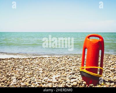 Orange Rettungsschwimmer am felsigen Strand mit ruhigem Meerblick und ohne Rettungsschwimmer. Statischer Leerraum vintage Copypaste Hintergrund Sicherheitskonzept Stockfoto