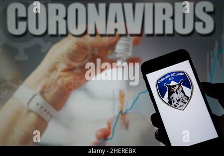 Foto vom 09-01-2021 des Oldham Athletic AFC-Logos auf einem Mobiltelefon mit einer Coronavirus-Illustration auf einem Monitor im Hintergrund. Das zwei-Spiel der Sky Bet League zwischen Oldham und Leyton Orient im Boundary Park am Samstag wurde aufgrund der Anzahl der Verletzungen und der positiven Covid-19-Fälle innerhalb der Heimmannschaft verschoben. Ausgabedatum: Mittwoch, 12. Januar 2022. Stockfoto