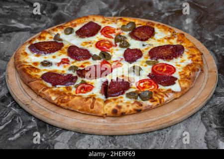 Pizza mit grünen Oliven, türkischer Wurst und Käse auf einem Schneidebrett Stockfoto