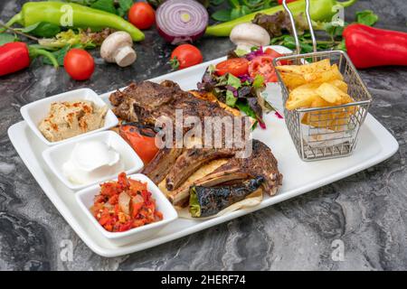 Gegrillte Lammkoteletts mit pommes Frites und Vorspeisen auf einem weißen Porzellanteller Stockfoto