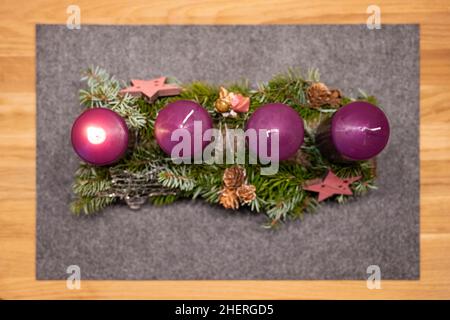 Violette Adventskerzen mit Ästen, Sternen und Tannenzapfen auf einem Filzkissen Stockfoto