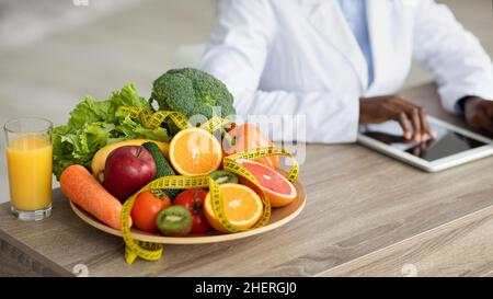 afroamerikanische Ernährungsberaterin arbeitet an einer digitalen Tablette, zählt Kalorien oder schreibt einen Diätplan Stockfoto