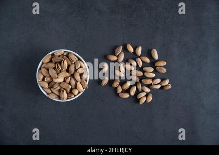 Pistazien in Schale und verteilt auf Beton, Stein Hintergrund. Geröstete und geschälte Pistazien von oben oder flach liegend. Gesunde Snacks. Stockfoto