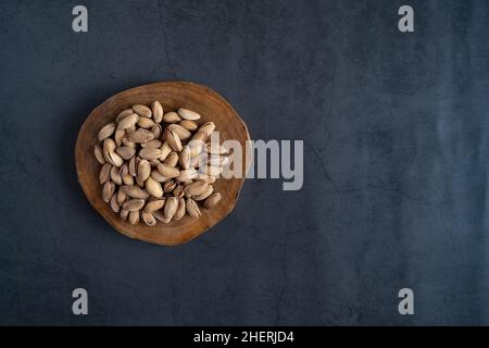 Pistazien auf Servierbrett. Geröstete und geschälte Pistazien auf Beton, Steingrund. Flach liegend, Draufsicht. Gesunde, leckere Snacks. Stockfoto