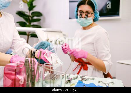 Verschwommenes Foto einer Zahnärztin, die ein Fernglas mit einer Lupe und einer medizinischen Maske bei ihrer Arbeit in der Zahnarztpraxis trägt, mit der Werkzeuge arbeiten Stockfoto