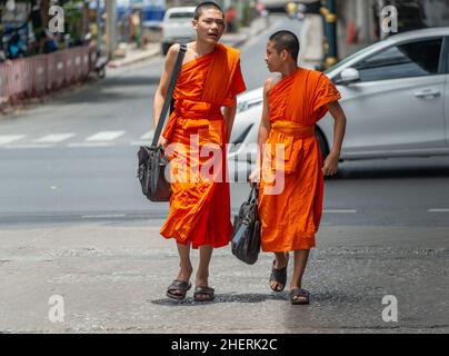 Zwei junge Mönche, die in Bangkok eine Straße entlang gehen. Vorderansicht. Stockfoto