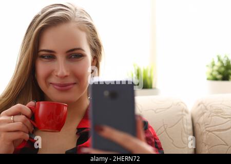 Junge schöne Frau trinkt Kaffee und schaut ins Smartphone Stockfoto
