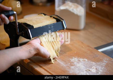 Von Hand selbst gemachte Nudeln mit Maschine auf Holz und Mehl Stockfoto