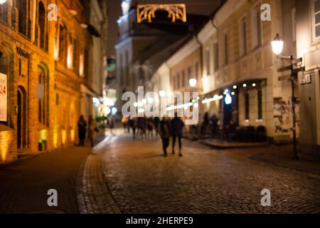 Fußgängerzone am Abend verschwommener Hintergrund. Menschen, die in der Altstadt auf einer gepflasterten Straße spazieren Stockfoto