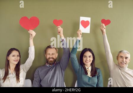 Gruppe lächelnder Menschen, die rote herzförmige Valentinstag- oder Grußkarten hochhalten Stockfoto